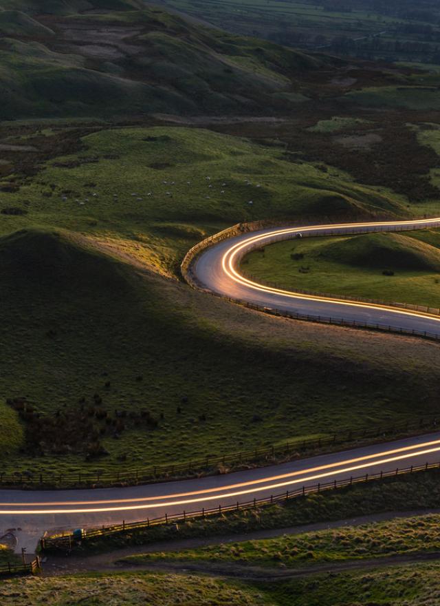 Winding curvy rural road with light trail from headlights leading through countryside.