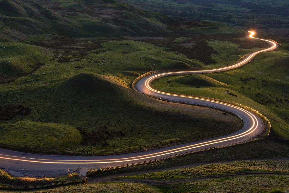 Winding curvy rural road with light trail from headlights leading through countryside.