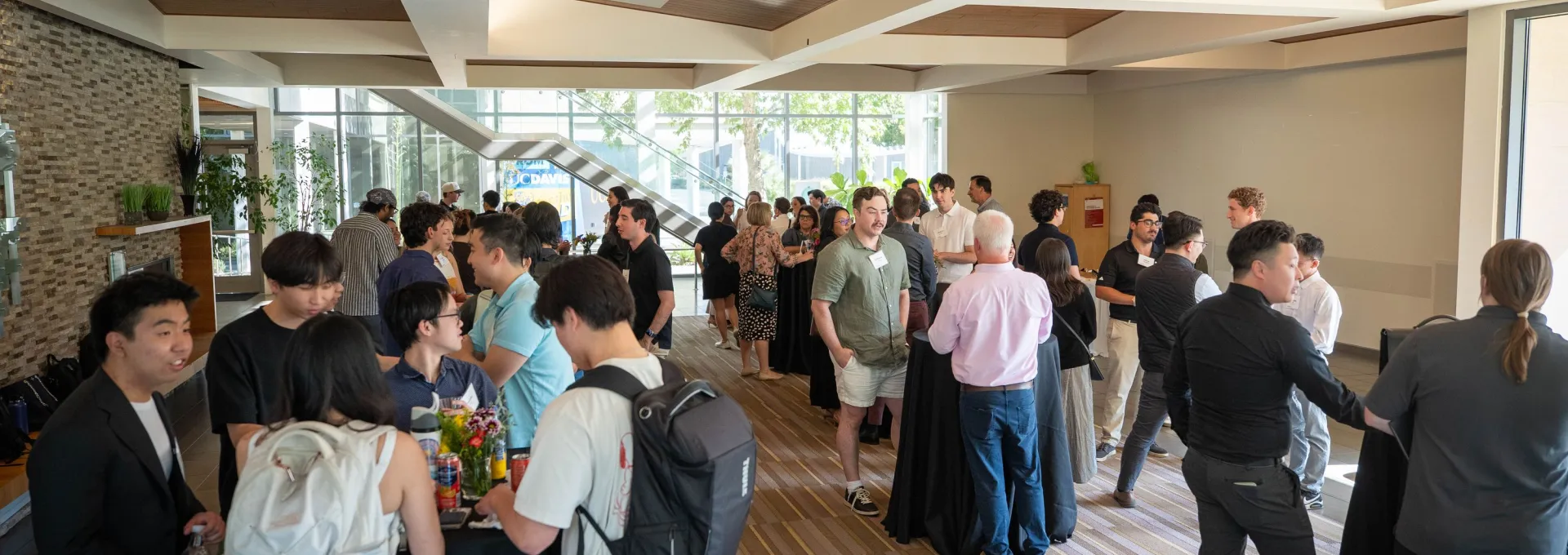 A group of people gather in a well-lit room, talking and mingling around cocktail tables during a casual event or networking session.