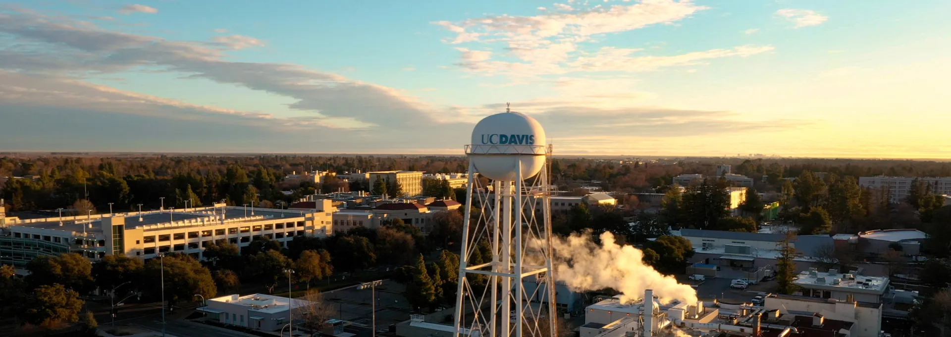 Aerial view of the UC Davis water tower at sunrise, with a nearby building emitting steam.