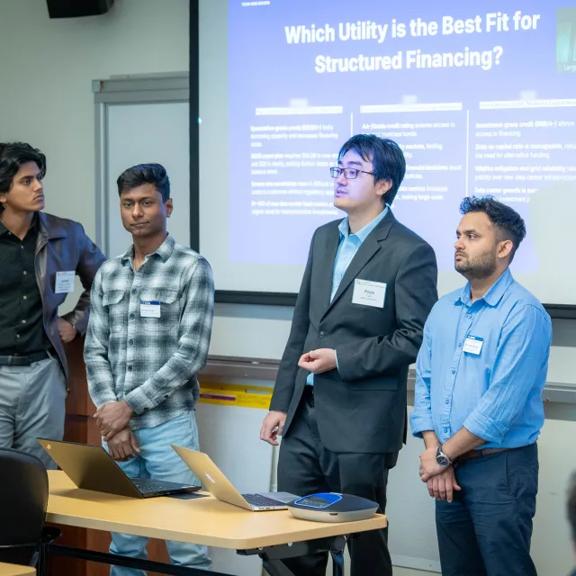 Four GSM students giving a presentation in front of a projector and screen