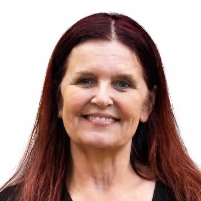 A woman with long reddish-brown hair and light skin smiles at the camera against a plain white background.
