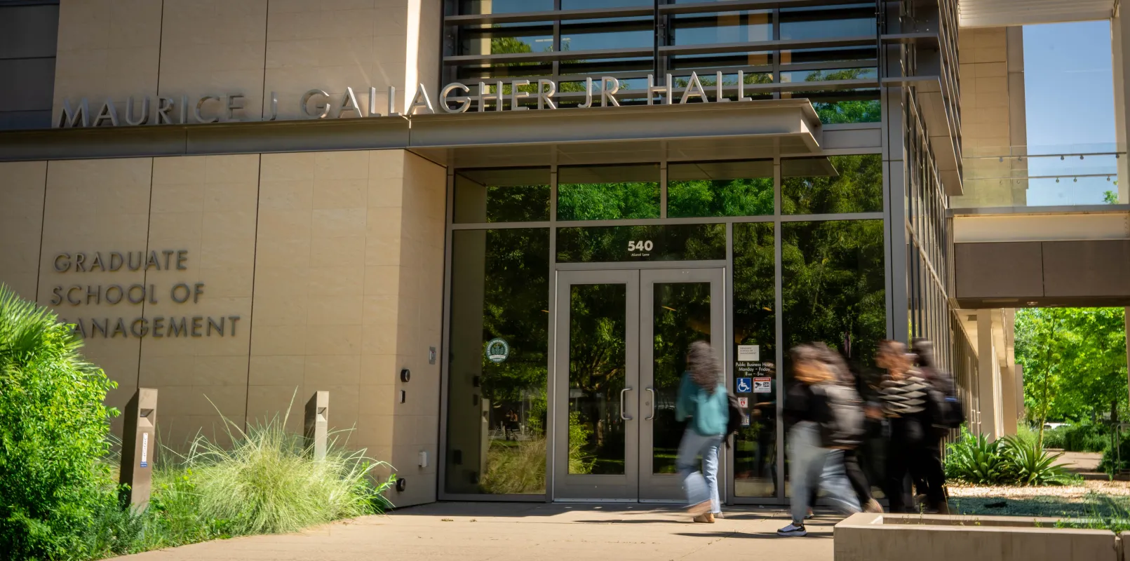 Students walk past the entrance of Maurice J. Gallagher Jr. Hall, Graduate School of Management, on a sunny day.