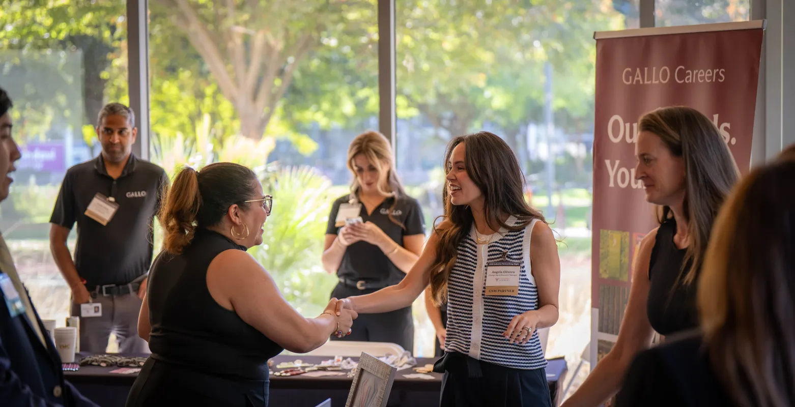 Two women shaking hands at a career fair booth branded with Gallo Careers.