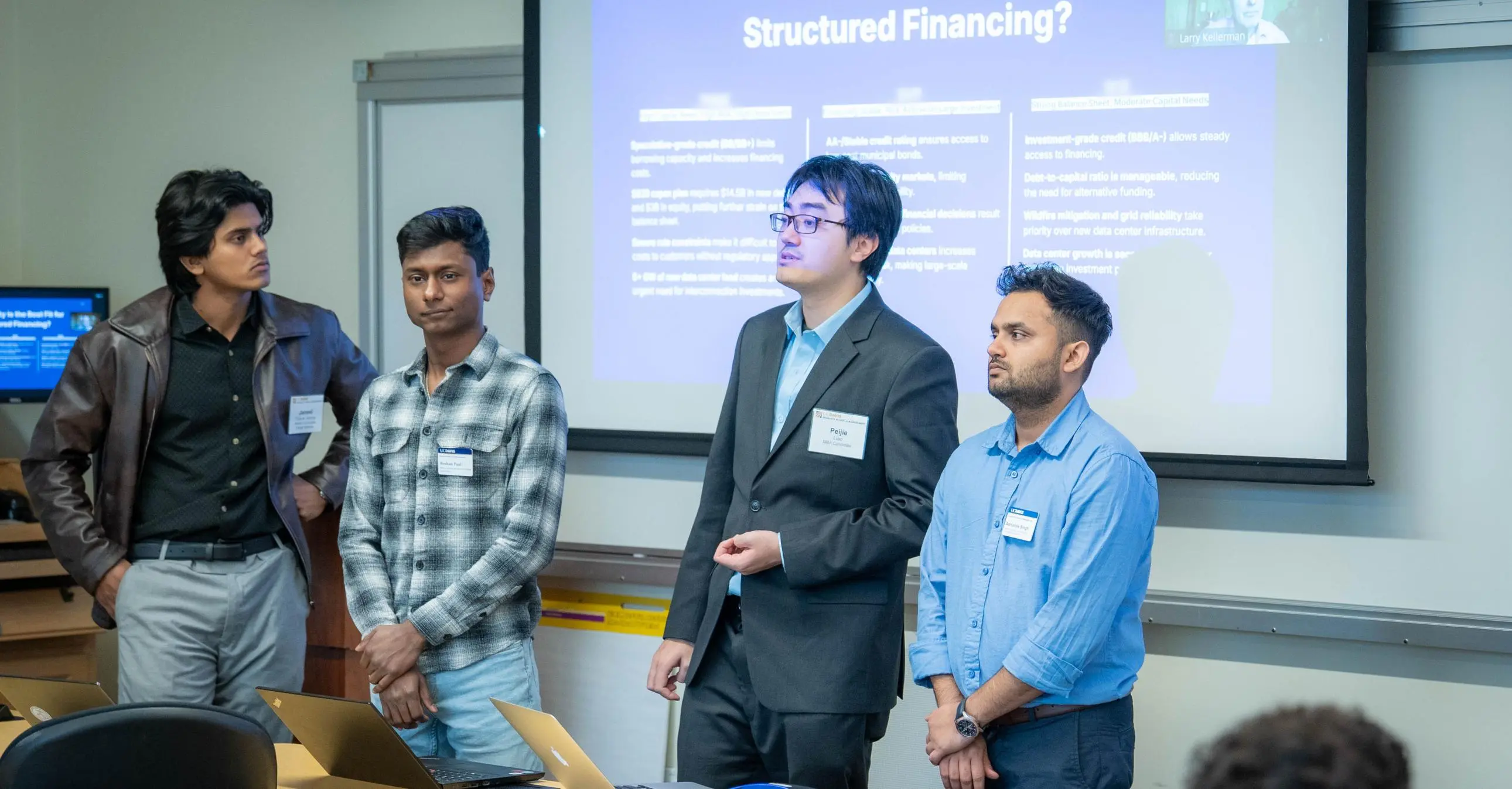 Four GSM students giving a presentation in front of a projector and screen