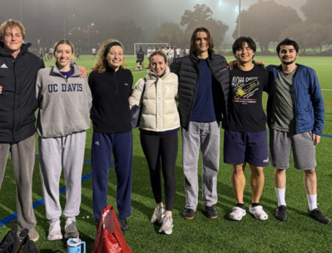 A group of UC Davis students stand together on a foggy soccer field at night, smiling after an intramural game.