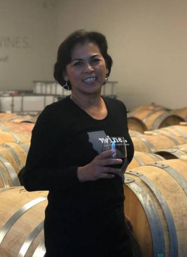 Christy Serrato with a glass of wine in front of wine barrels