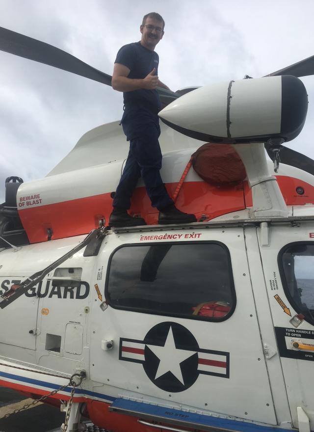 Person standing on top of a parked U.S. Coast Guard helicopter