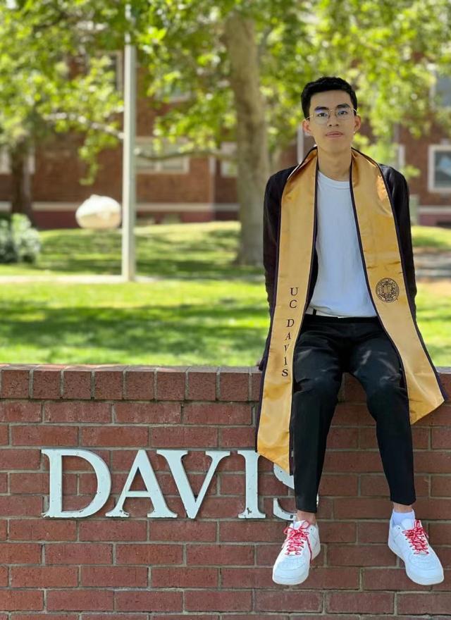 Shiwei Zhang sitting on a UC Davis sign