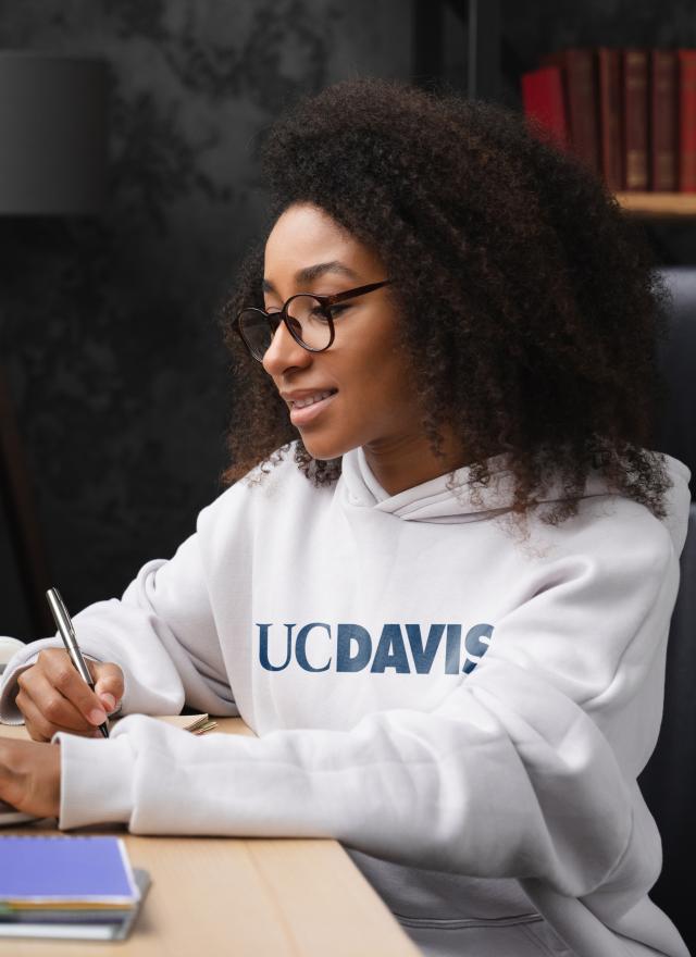 Woman sitting at laptop wearing a UC Davis sweatshirt