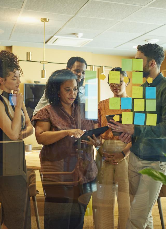 A group of diverse professionals brainstorm ideas in a modern office space. They are using sticky notes to organize their thoughts.