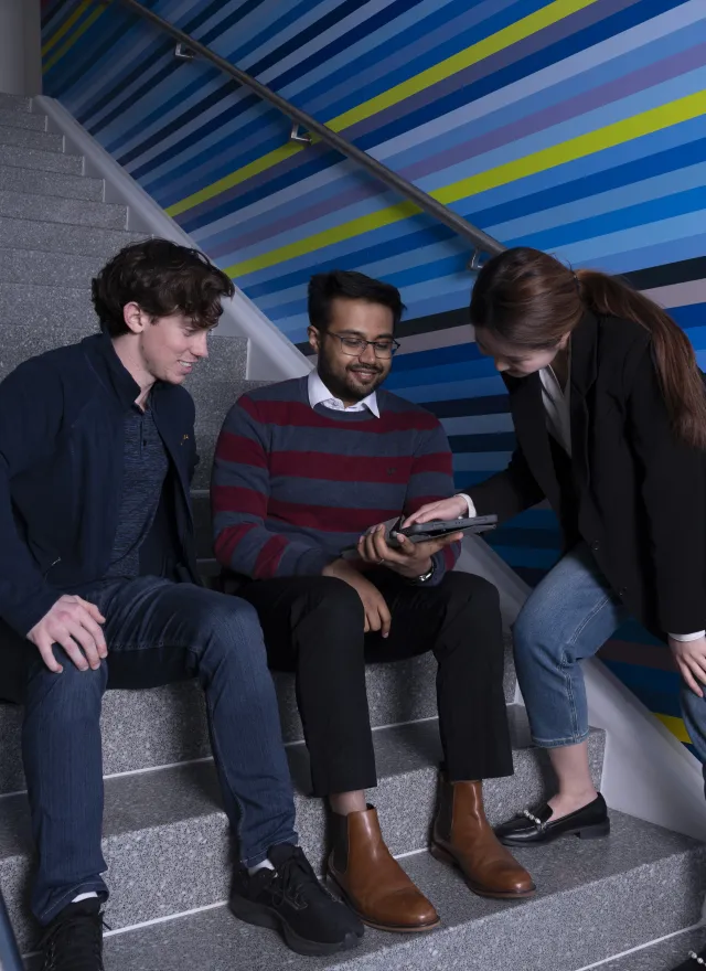 Group of individuals sitting on stairs looking at a tablet