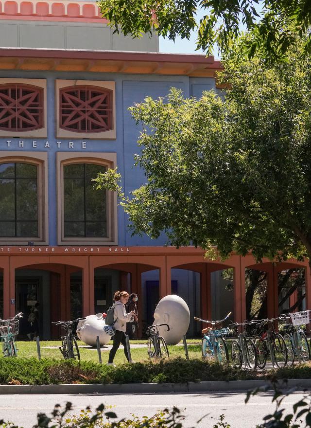 Student walking in front of a building and two egghead sculptures