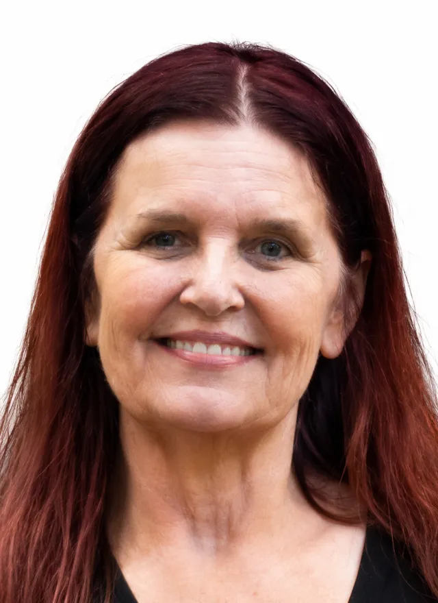 A woman with long reddish-brown hair and light skin smiles at the camera against a plain white background.