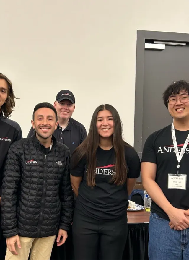 Five people in Andersen-branded apparel standing in front of an Andersen recruitment banner.
