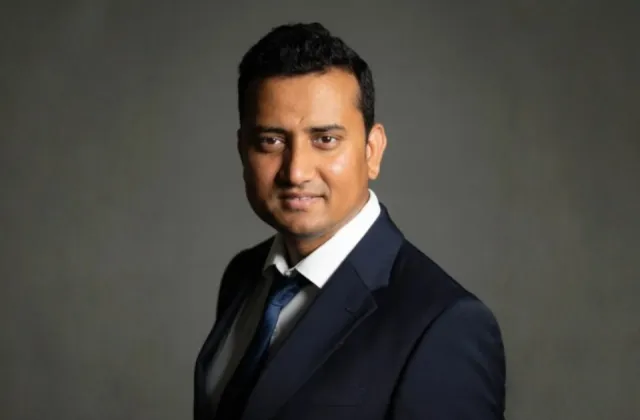 A man in a suit and tie poses for a portrait against a gray background.