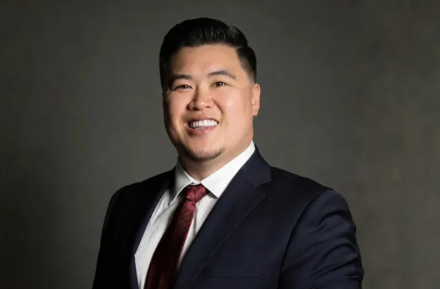 Headshot of a smiling man in a dark suit, white shirt, and maroon tie.