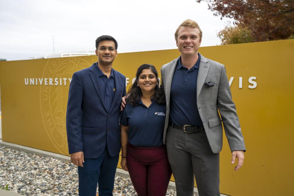 Three individuals standing in front of UC Davis sign