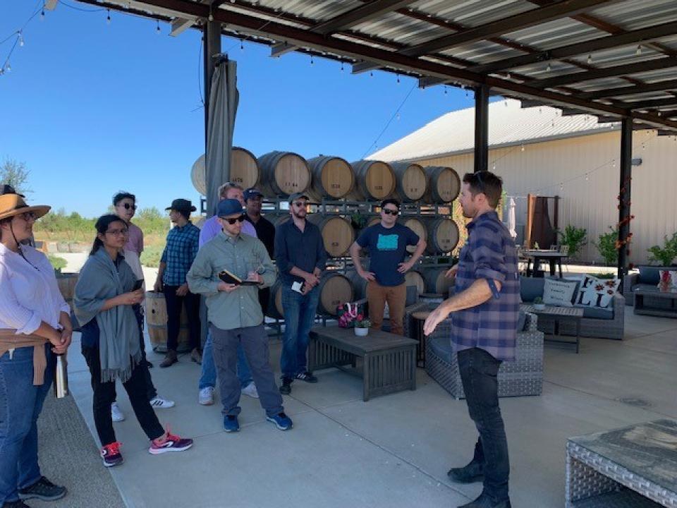 Group of people standing in front of wine barrels.