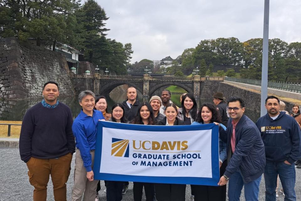 a group of MBA students holding up a UC Davis banner in Japan