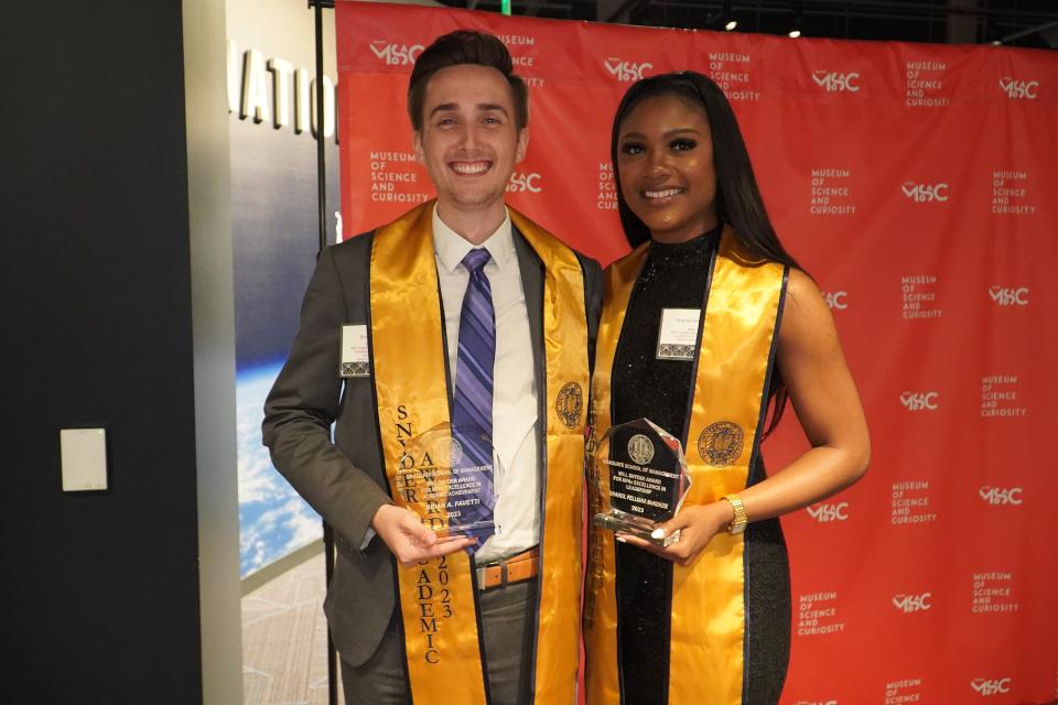 Brian Favetti and Shaneil Mckenzie wear graduate stoles and hold up student awards