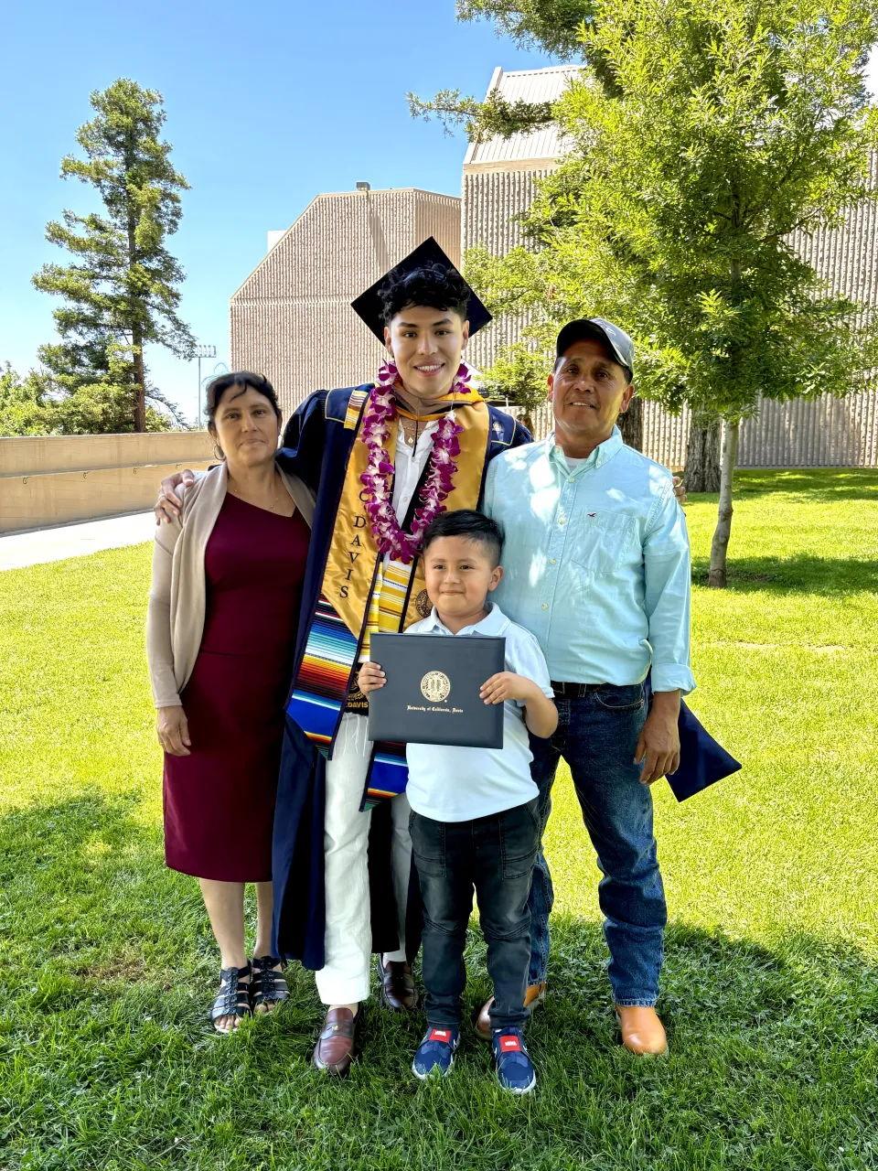 Eduardo Casarubias donning graduation robe and cap and pictured with his family