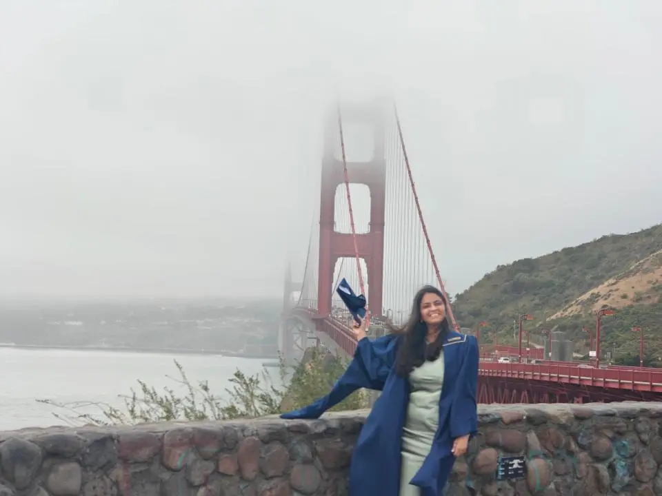 Shrishti Gupta wearing graduation robe in front of the Golden Gate bridge