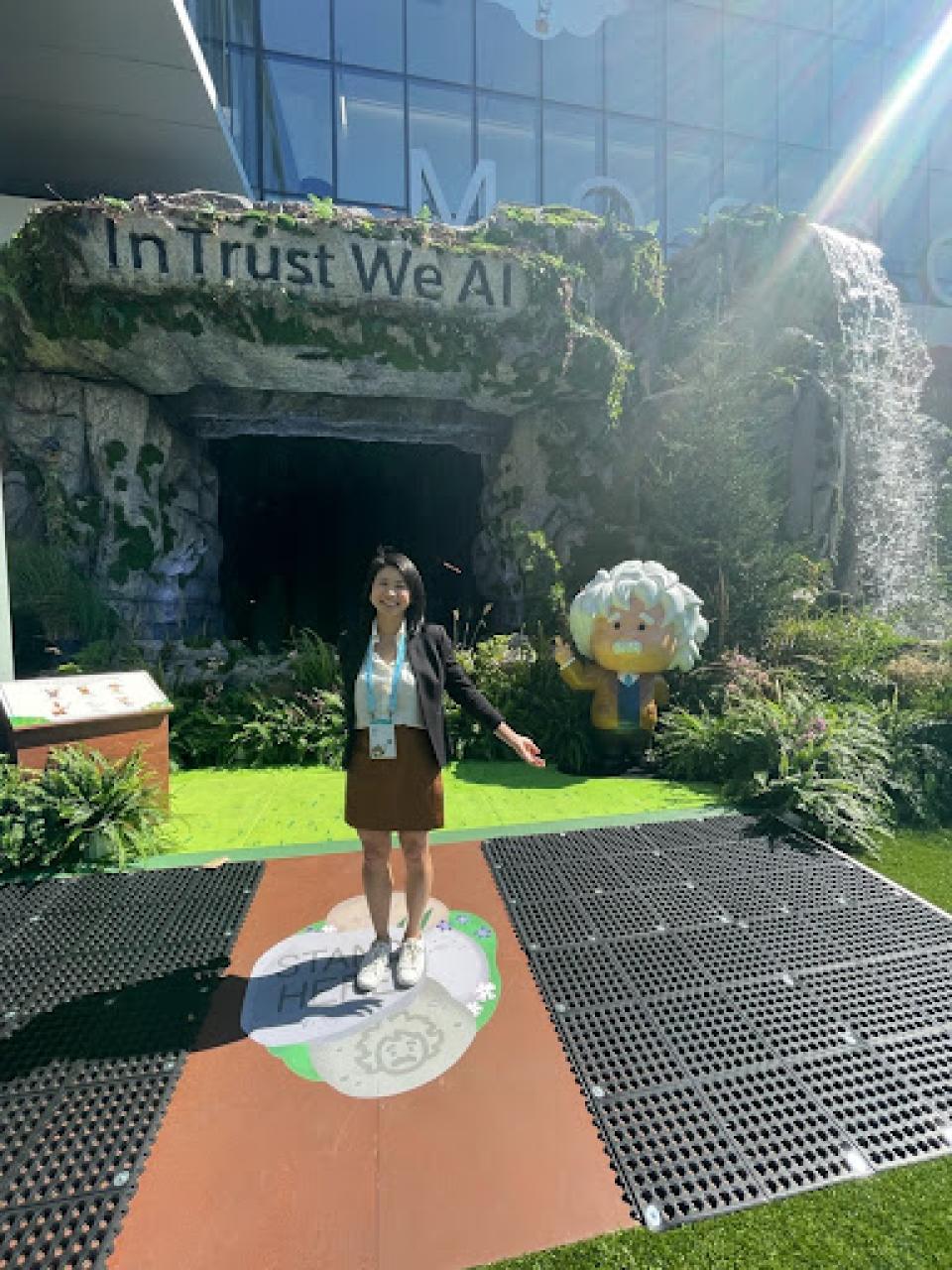 Linda Trinh standing outside, in front of a sign that says, "In Trust We AI"