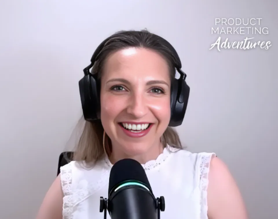 Woman wearing headphones and a white top speaks into a microphone against a light background with the text “PRODUCT MARKETING Adventures” in the top right corner.
