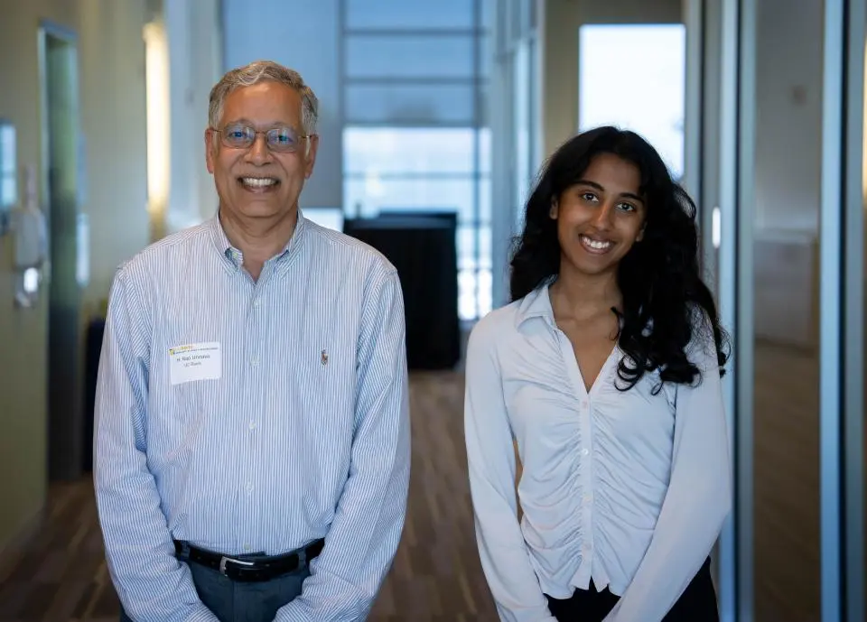 Dean Unnava and Rachel Johnson side by side in a hallway, both wearing light-colored shirts and smiling at the camera.