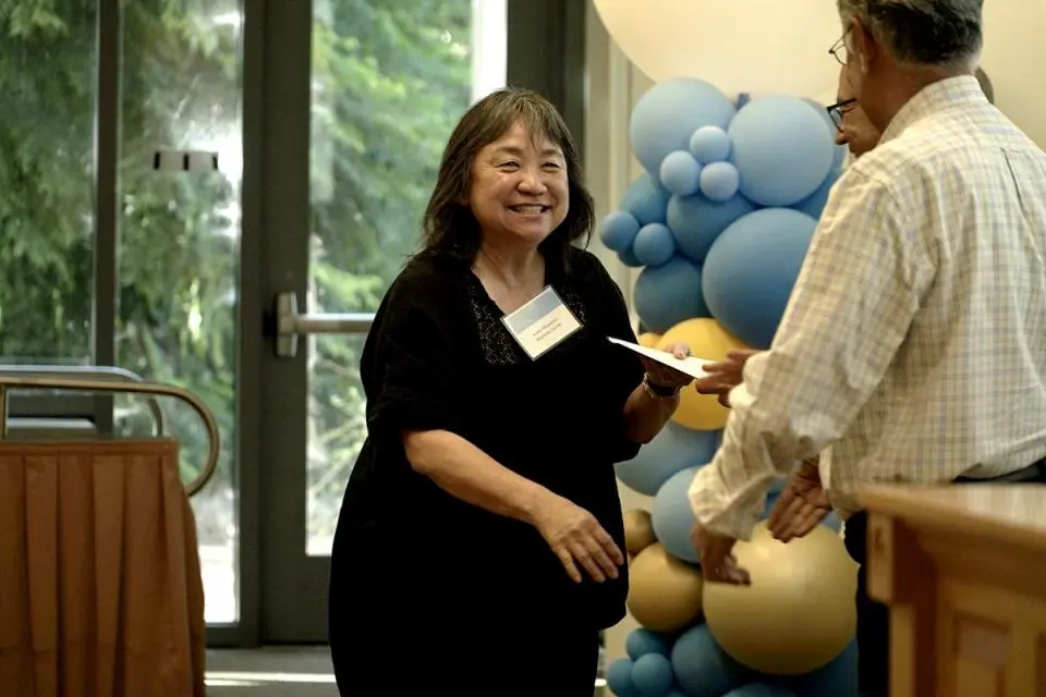 A woman smiles while accepting an envelope from a man at an indoor event with a balloon display in the background.