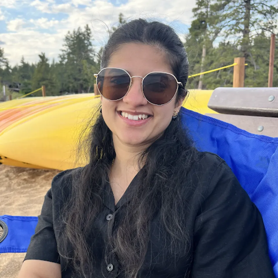 Avani Karandikar smiles at the camera while sitting on a blue beach chair near a yellow kayak outdoors.