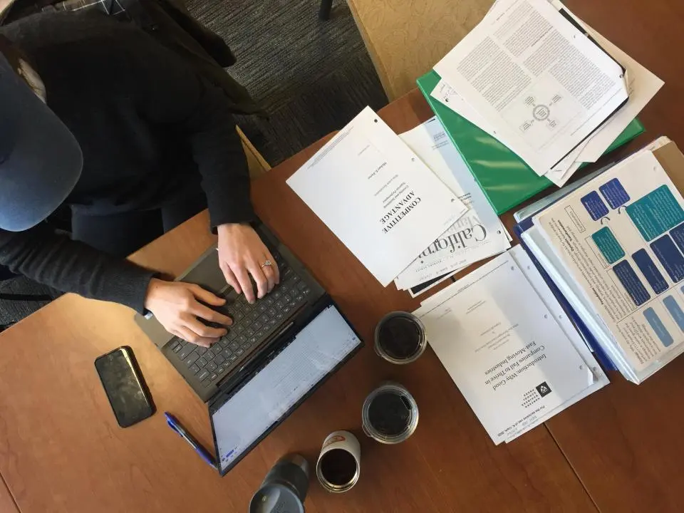 A person working at a laptop with stacks of papers around them
