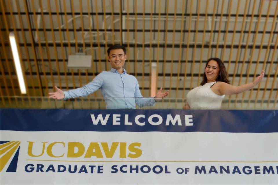 Two individuals posing in front of UC Davis Graduate School of Management banner