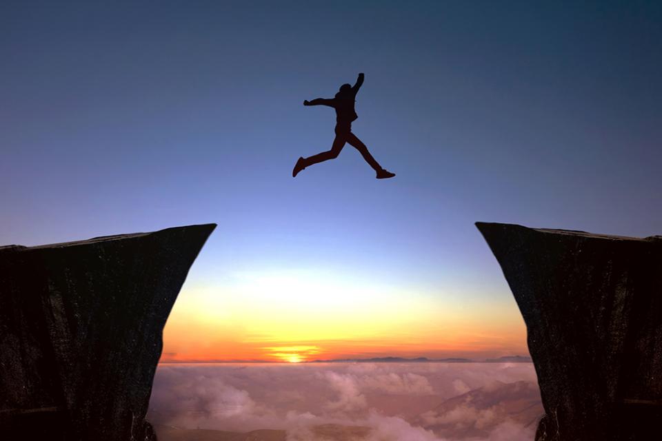 photo of person leaping across two cliffs