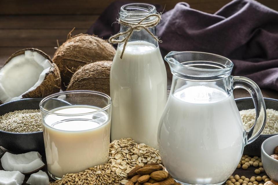 A glass, a bottle and a jug of milk surrounded by tree nuts, seeds, grains and coconuts. 