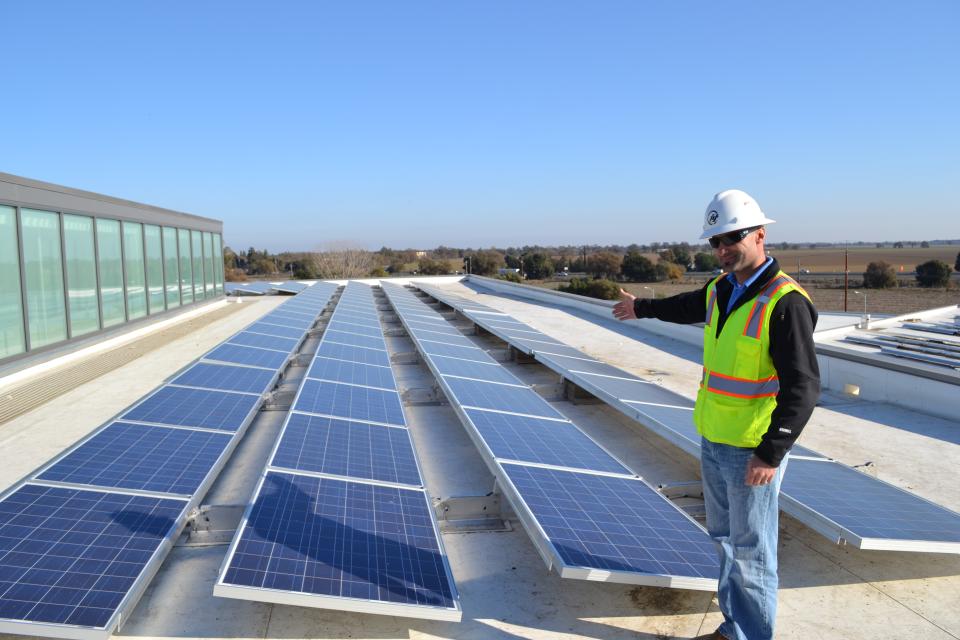 Solar array atop Gallagher Hall at UC Davis with technician pointing