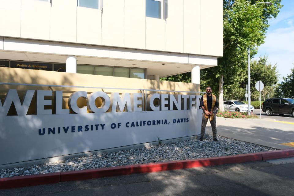 Sanjay Puri standing in front of UC Davis Welcome Center, wearing a graduation stole